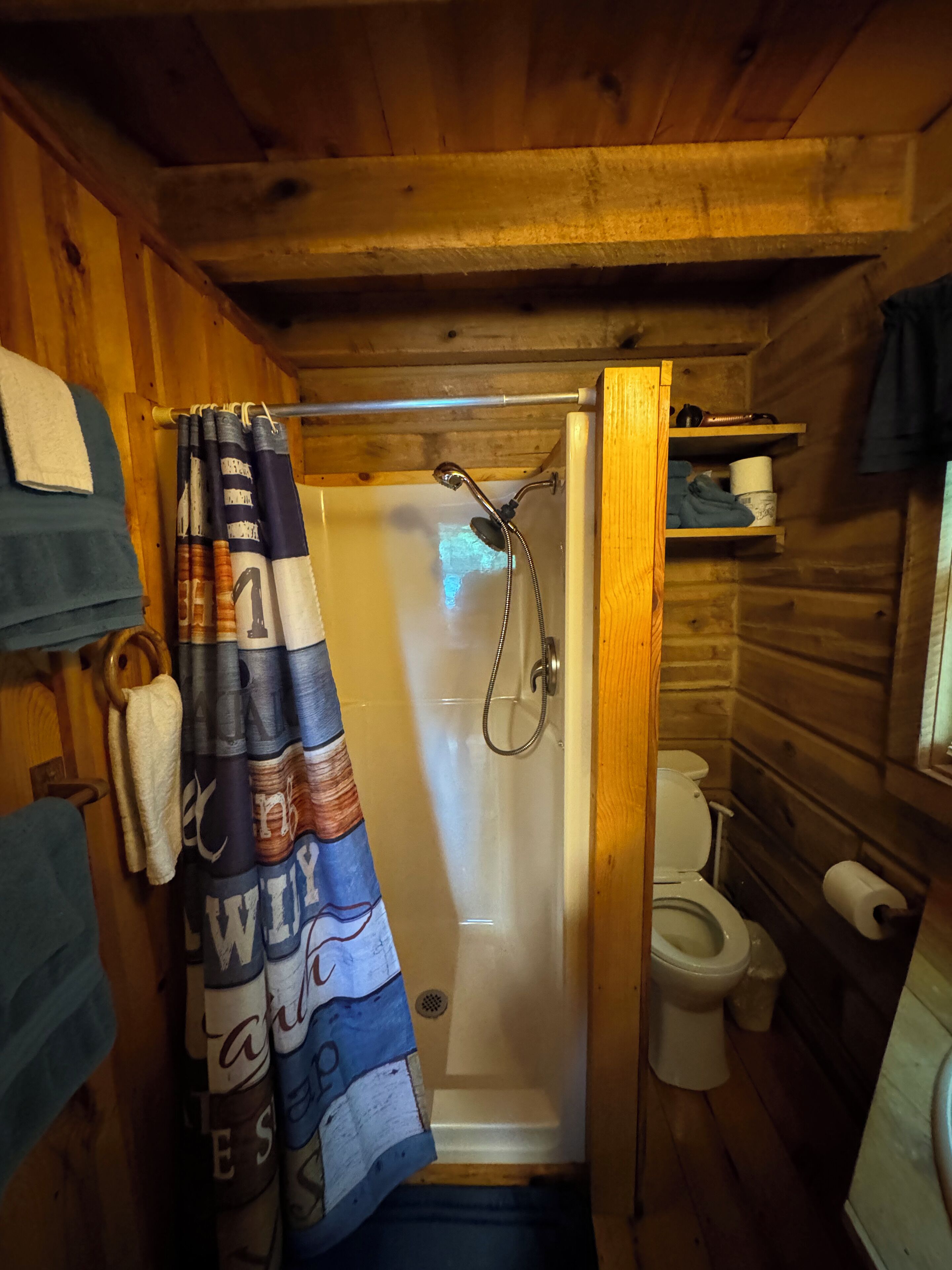 Een houten badkamer in een vakantiehuisje, met een douche, toilet en een handdoekhouder.
