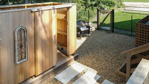 A wooden outdoor storage unit with a sliding door, a bench, and a fenced area with a gravel path.