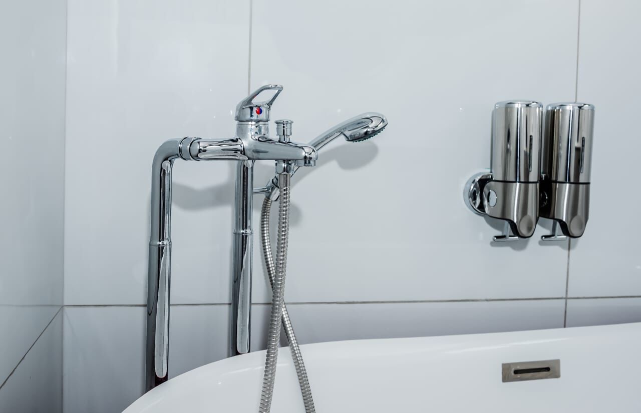 A bathroom with a chrome showerhead, a handheld shower, and a wall-mounted faucet.