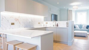 A modern kitchen with marble countertops, wooden stools, and light blue cabinetry.