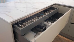 A kitchen with a marble countertop and a built-in drawer with utensils and appliances.
