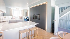 A modern kitchen with a marble island, wooden stools, and a built-in oven.