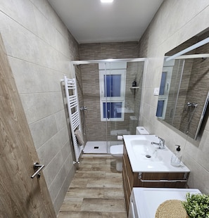 Bathroom features a shower, toilet, and sink with a glass door and window.