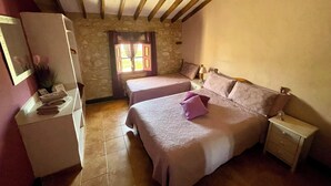 A bedroom with two beds, a dresser, a nightstand, a window with curtains, and a stone wall. - Self catering Accommodation for the Larger Group (Ubeda)