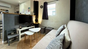 Un dormitorio moderno con cama, escritorio, silla, mesita, espejo, reloj y ventana con cortinas.