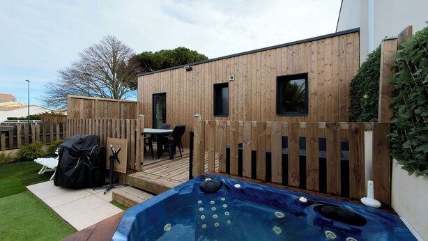 Una terraza de madera con un jacuzzi, una zona de barbacoa y una mesa de comedor con sillas.