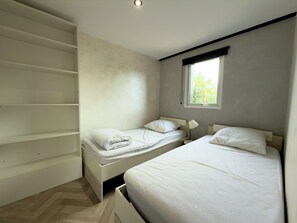 A bedroom with two beds, a window, and built-in shelving. - "Le refuge Sablais" Vacation Home with Air Conditioning and Jacuzzi (Les Sables-d'Olonne)
