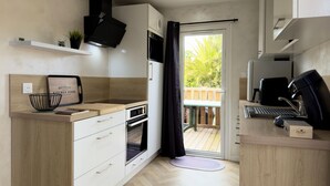Una cocina moderna con armarios de madera, horno empotrado, cafetera y vistas a una terraza de madera a través de una puerta de vidrio.
