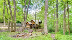 A cabin in a forest with a deck and stairs leading to a second level. - Log Cabin w/ Vaulted Great Room & Creek Near GSMNP (Sevierville)