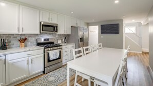 A modern kitchen with white cabinets, stainless steel appliances, and a dining area with a white table and chairs. - 1 Mi to Lake Erie: Family-Friendly Angola Home! (Angola)