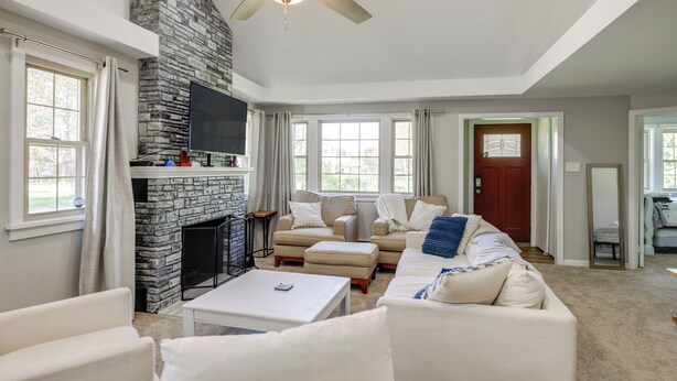 A living room with a stone fireplace, a ceiling fan, and a large window. - 1 Mi to Lake Erie: Family-Friendly Angola Home! (Angola)