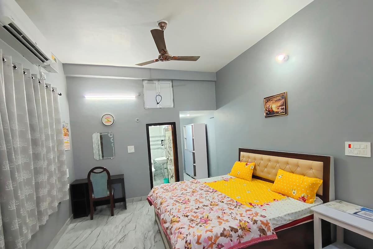 A bedroom with a bed, a ceiling fan, a nightstand, a mirror, and a bathroom door.