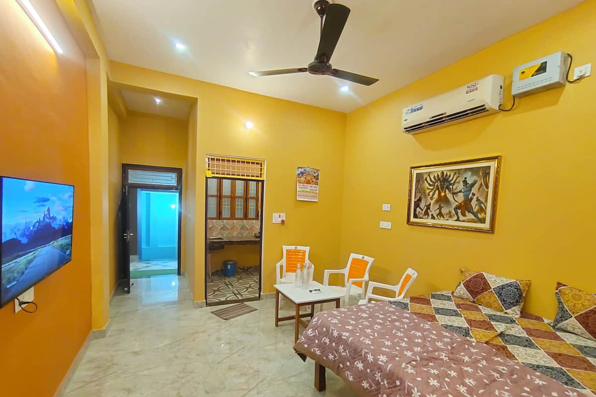 A hotel room with a bed, a desk, two chairs, a television, an air conditioner, and a ceiling fan.