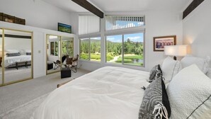 Ein Schlafzimmer mit einem großen Bett, einem Sessel, einem Spiegel und Blick auf einen Golfplatz.
