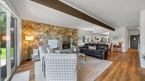 Ein geräumiges Wohnzimmer mit Steinwand, Kamin, einem schwarzen Ledersofa und einem Akzentstuhl mit Hundeprozessmuster.