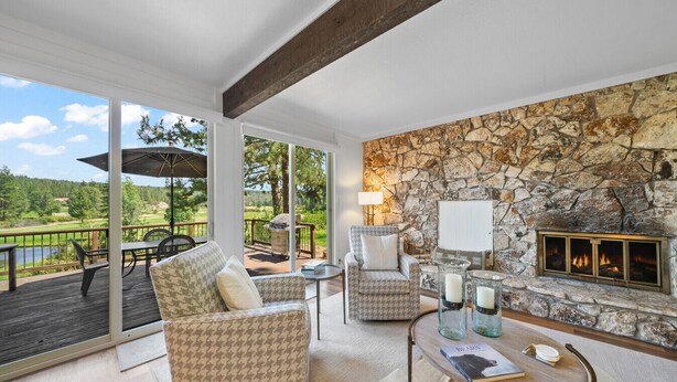 Ein gemütliches Wohnzimmer mit Kamin aus Stein, bequemen Sitzgelegenheiten und Blick auf einen Golfplatz.