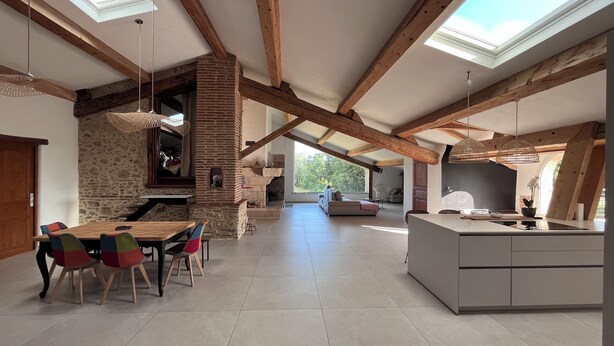 A spacious living area with exposed wooden beams, a stone fireplace, a dining table with colorful chairs, and a kitchen with a large island. - Domaine Villadomar: Farmhouse nestled in the heart of Thuir in the calm of its wooded grounds (thuir)