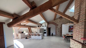 A spacious kitchen with a central island, exposed wooden beams, and a stone wall. - Domaine Villadomar: Farmhouse nestled in the heart of Thuir in the calm of its wooded grounds (thuir)