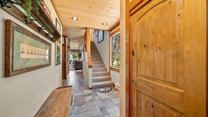 A wooden interior hallway with a staircase, framed pictures on the walls, and a wooden door.