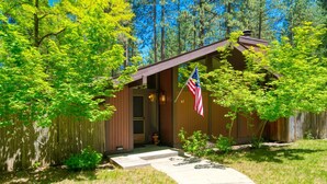 A wooden cabin with a porch, a flag, and a well-maintained lawn. - Nestled in the heart of Graeagle Meadows, Private Fenced Yard, Sleeps 6 (Graeagle)