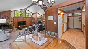 A spacious living room with a fireplace, a dining area with a wooden table, and a kitchen area visible through an open doorway. - Nestled in the heart of Graeagle Meadows, Private Fenced Yard, Sleeps 6 (Graeagle)