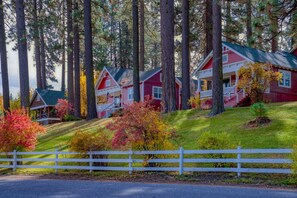 A row of red cabins with white trim, surrounded by tall trees and a white fence.