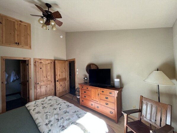 A bedroom with a bed, wooden wardrobe, television, lamp, and a ceiling fan.