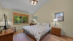 A bedroom with a bed, desk, and computer, a window with a view of greenery, a ceiling fan, and a framed picture on the wall. - Sophisticated Remodel, Single Level, Fenced Yard (Graeagle)