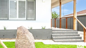 A modern house with a grey exterior, a large rock in the front yard, and a covered outdoor staircase leading to a balcony. - Granite Grove - Port Elliot (Port Elliot)