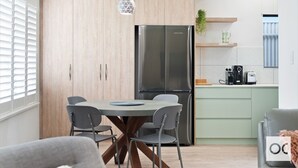 A modern kitchen with a central island, stainless steel appliances, and a dining area with a round table and chairs. - Granite Grove - Port Elliot (Port Elliot)