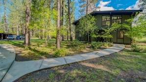 A house surrounded by tall trees and a concrete pathway leading to it. - Enjoy the beauty of Graeagle Meadows Golf Course and from this charming mountain retreat! (Graeagle)