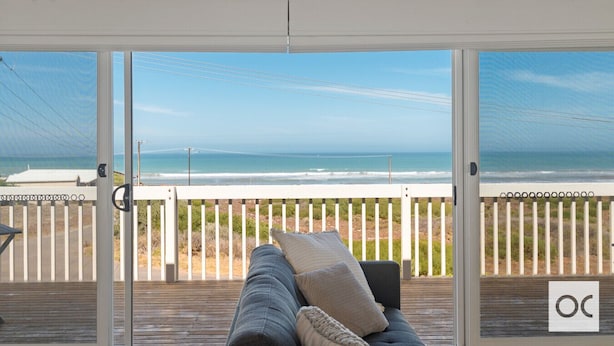 A room with a view of the ocean, a wooden deck, and a white railing.