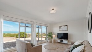 A spacious living room with large windows, a flat-screen TV, and a comfortable seating area.