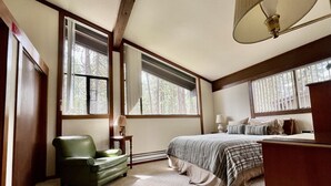 A bedroom with a large bed, a green armchair, and a desk with a lamp. - Vacation retreat for golf and enthusiasts and families alike! (Graeagle)