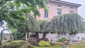 Ein Garten mit einem rosa Gebäude, einem Baum und einer Bank.