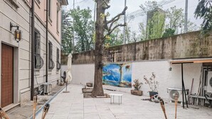 Eine Terrasse im Freien mit gefliestem Boden, einem Baum, einem Wandgemälde und Topfpflanzen.