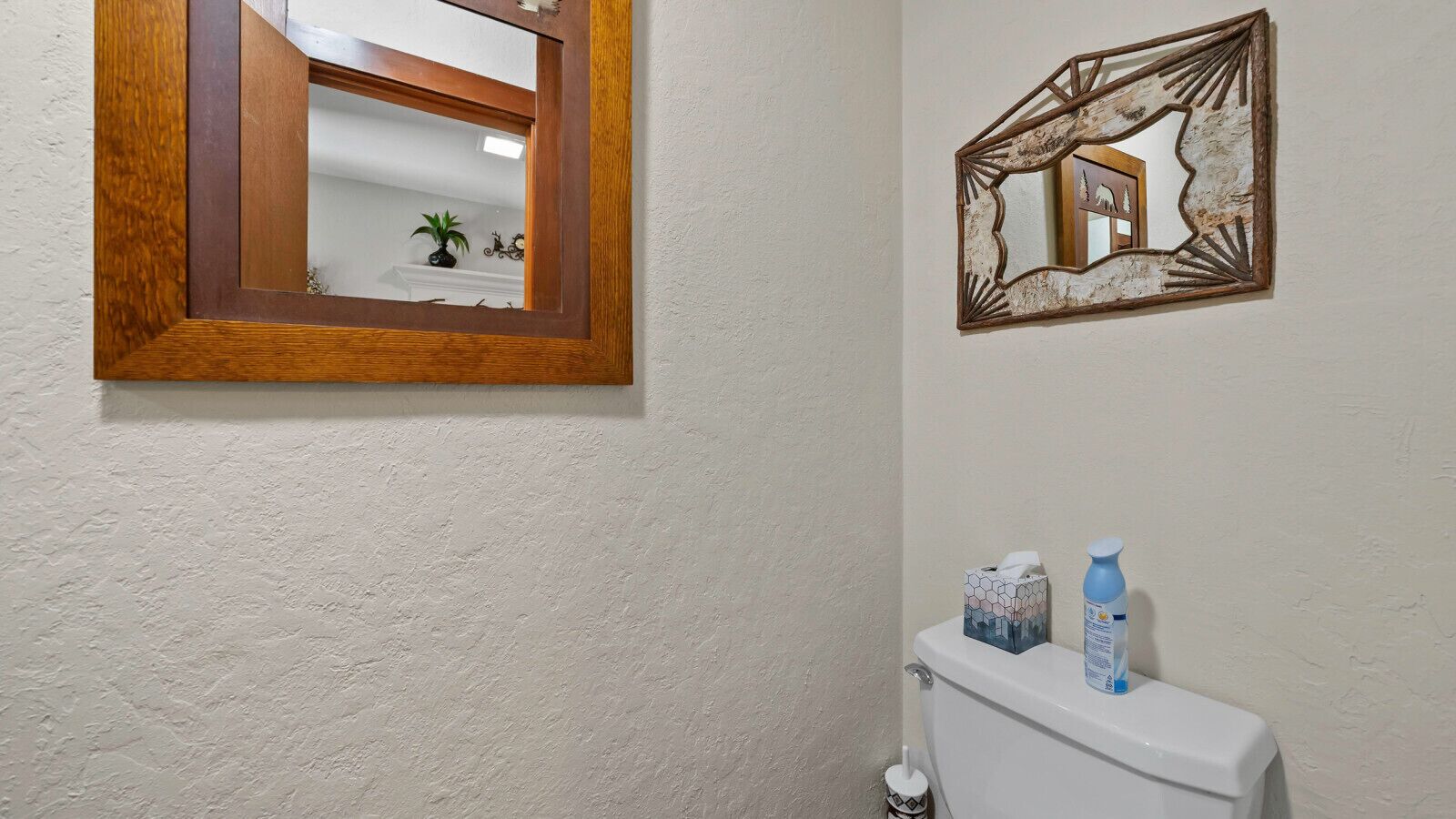 A bathroom with a wooden-framed mirror, a toilet, and a wall-mounted shelf with toiletries.