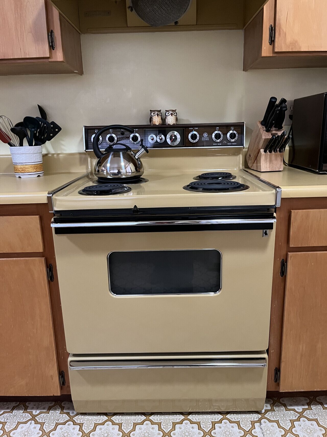 A kitchen with a beige stove, wooden cabinets, and a tiled floor.