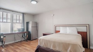 Hotellihuone, jossa on sänky, työpöytä, jääkaappi ja ikkuna.