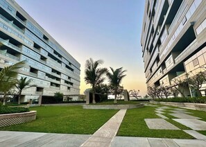 A modern building with multiple floors and balconies, surrounded by a well-maintained lawn and palm trees.