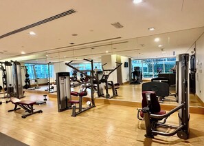 A gym with various exercise machines, large windows, and a wooden floor.