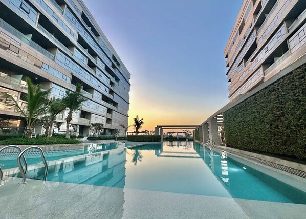 A modern building with a swimming pool, surrounded by greenery and palm trees.