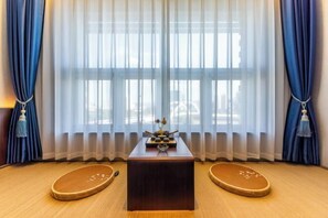 Um quarto com piso de madeira, uma mesa central com um objeto decorativo e dois banquinhos de madeira.