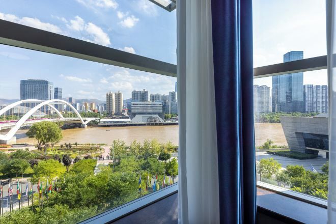 Blick aus einem Fenster auf ein modernes Gebäude, einen Fluss und eine Brücke.