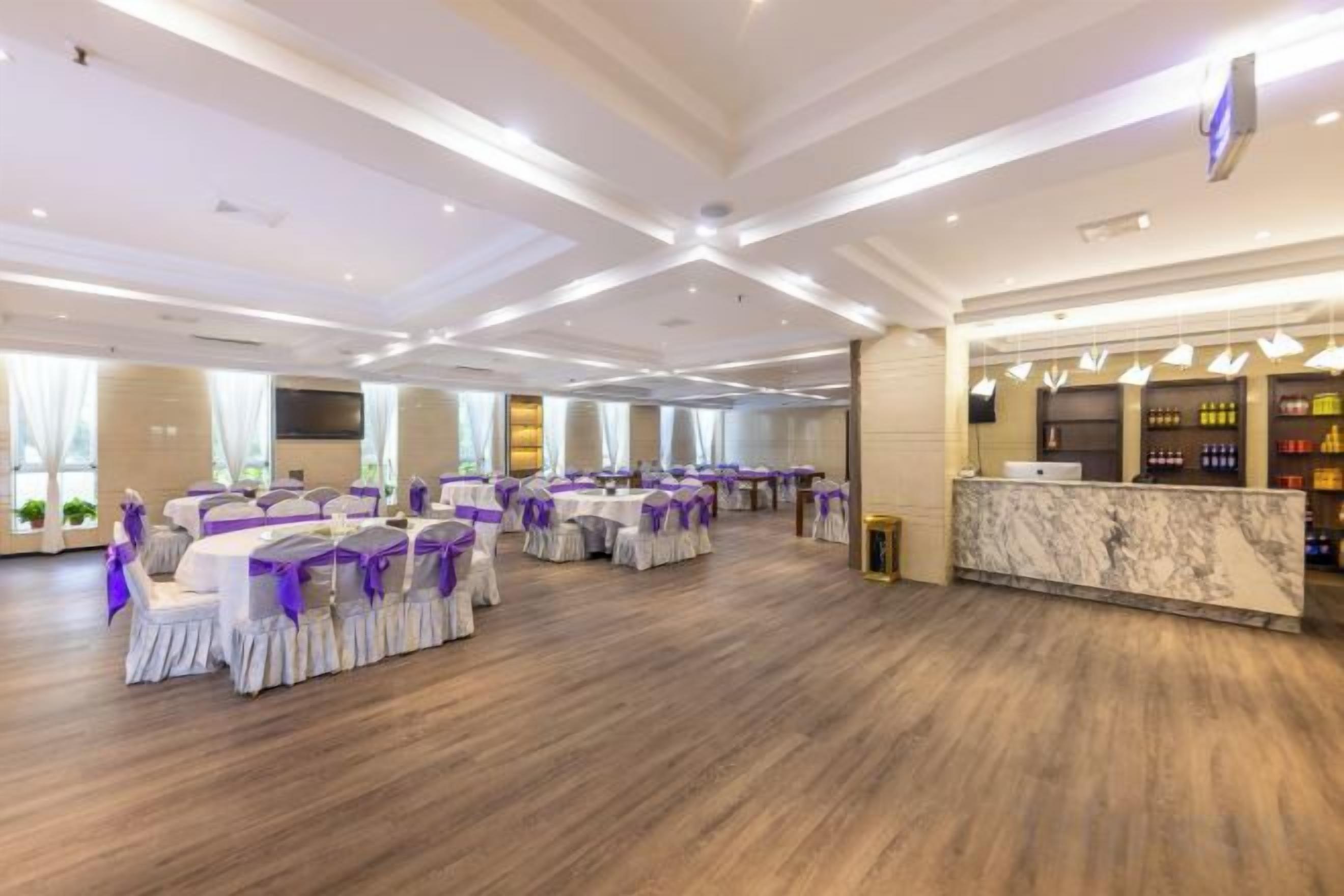 A spacious banquet hall with round tables and chairs, a reception area, and a marble counter.