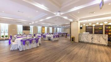 A spacious banquet hall with round tables and chairs, a reception area, and a marble counter.
