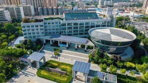 Ein modernes Gebäude mit einer kreisförmigen Glasstruktur, umgeben von Pflanzen und Solaranlagen.