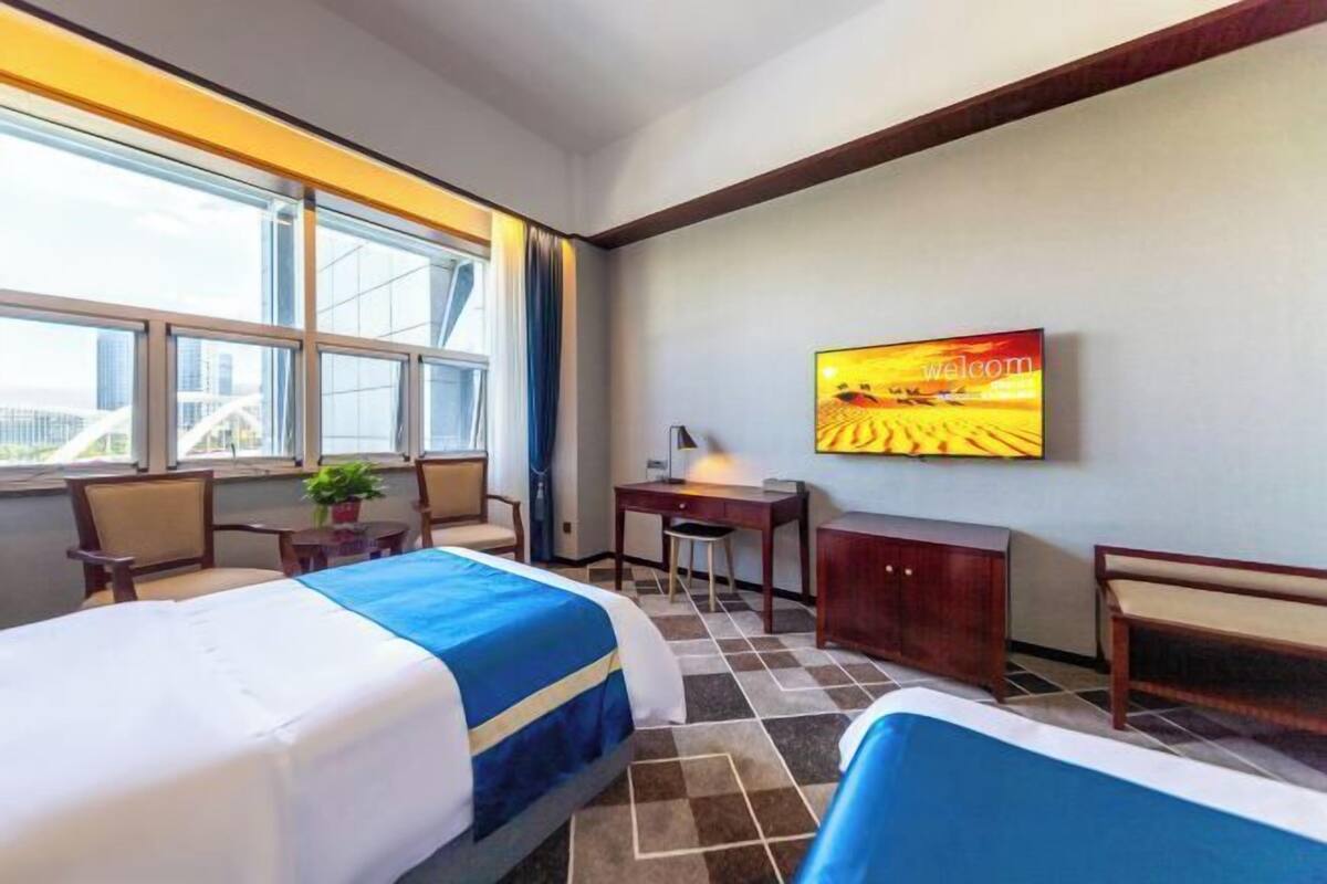 A hotel room with two beds, a desk, a chair, a TV, and a window with a city view.