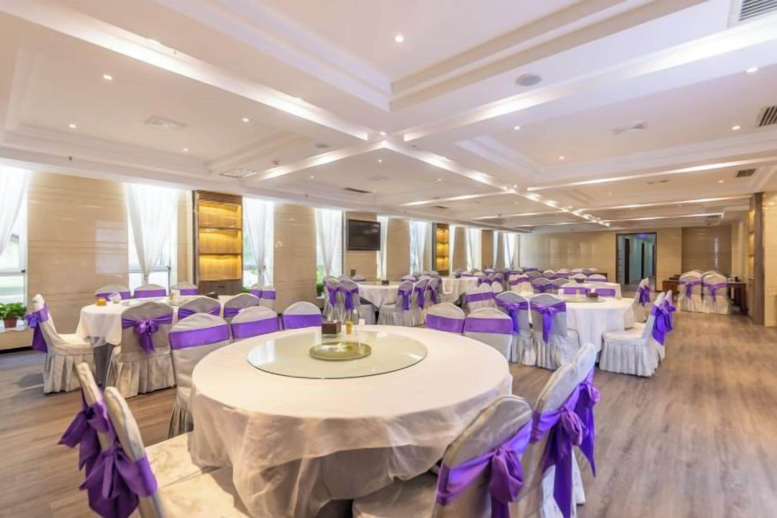 A banquet hall with round tables, chairs, and purple sashes.