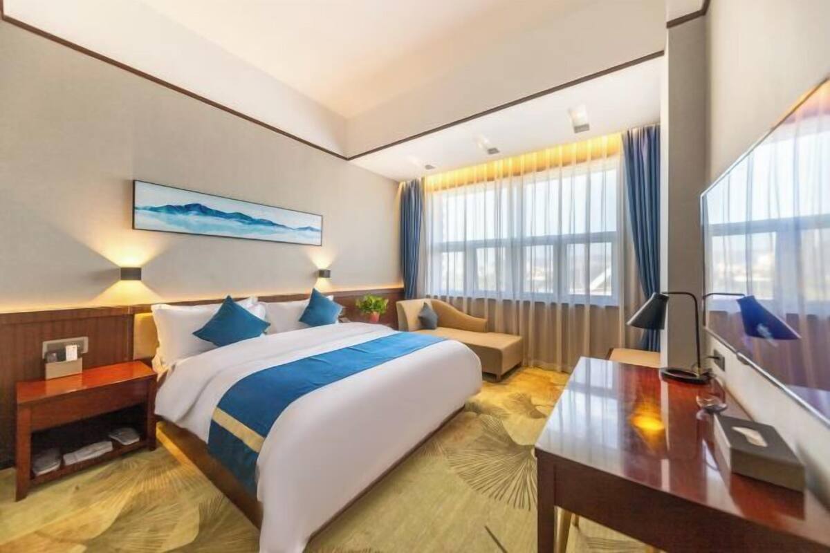 A hotel room with a large bed, a desk, a chair, a TV, and a window with curtains.
